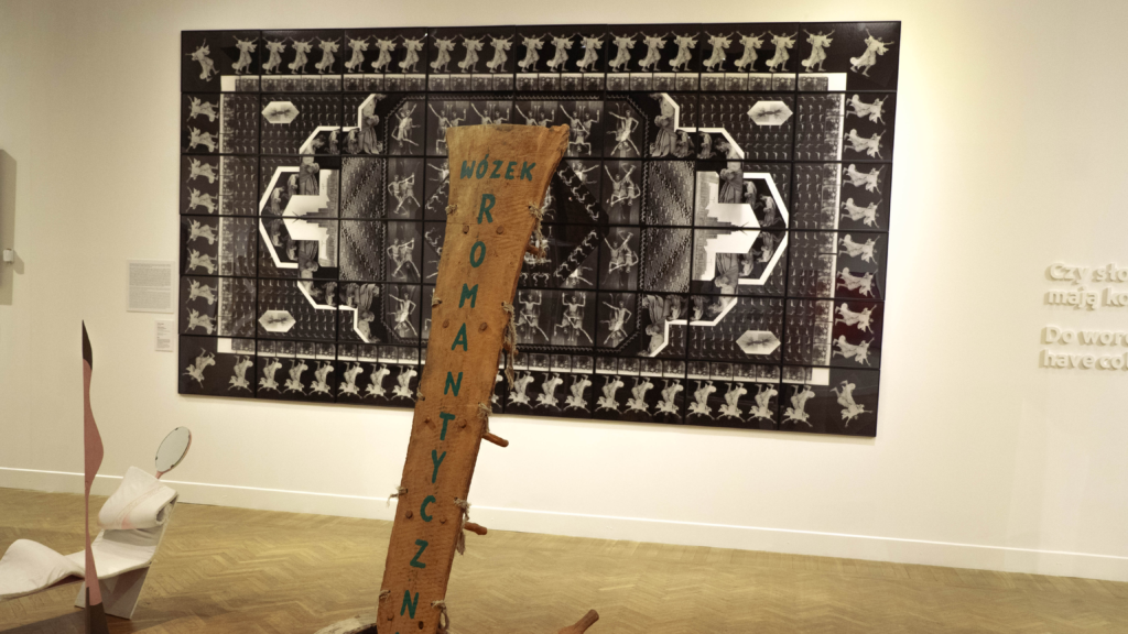 Instalacja "Wózek romantyczny", autorstwa Jerzego Beresia, składająca się z drewnianej deski na kółkach, z napisem tożsamym z tytułem dzieła